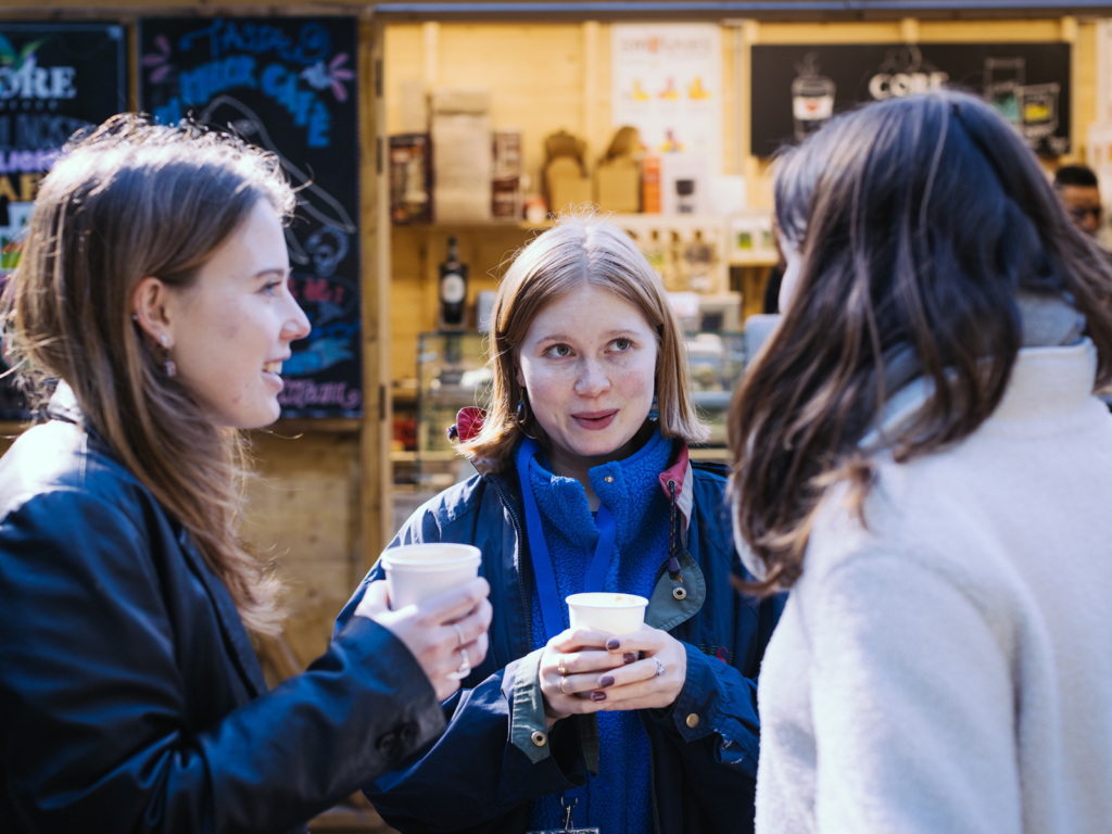 Three women talking and drinking a cup of coffee outside.