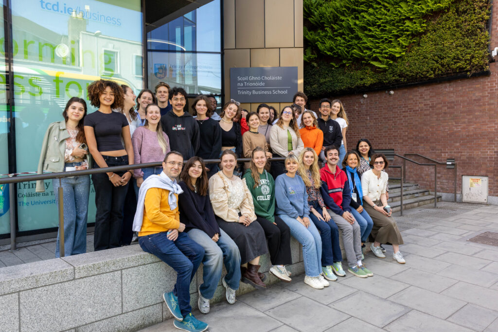 A large group of people stand and sit outside Trinity college Dublin's Business School