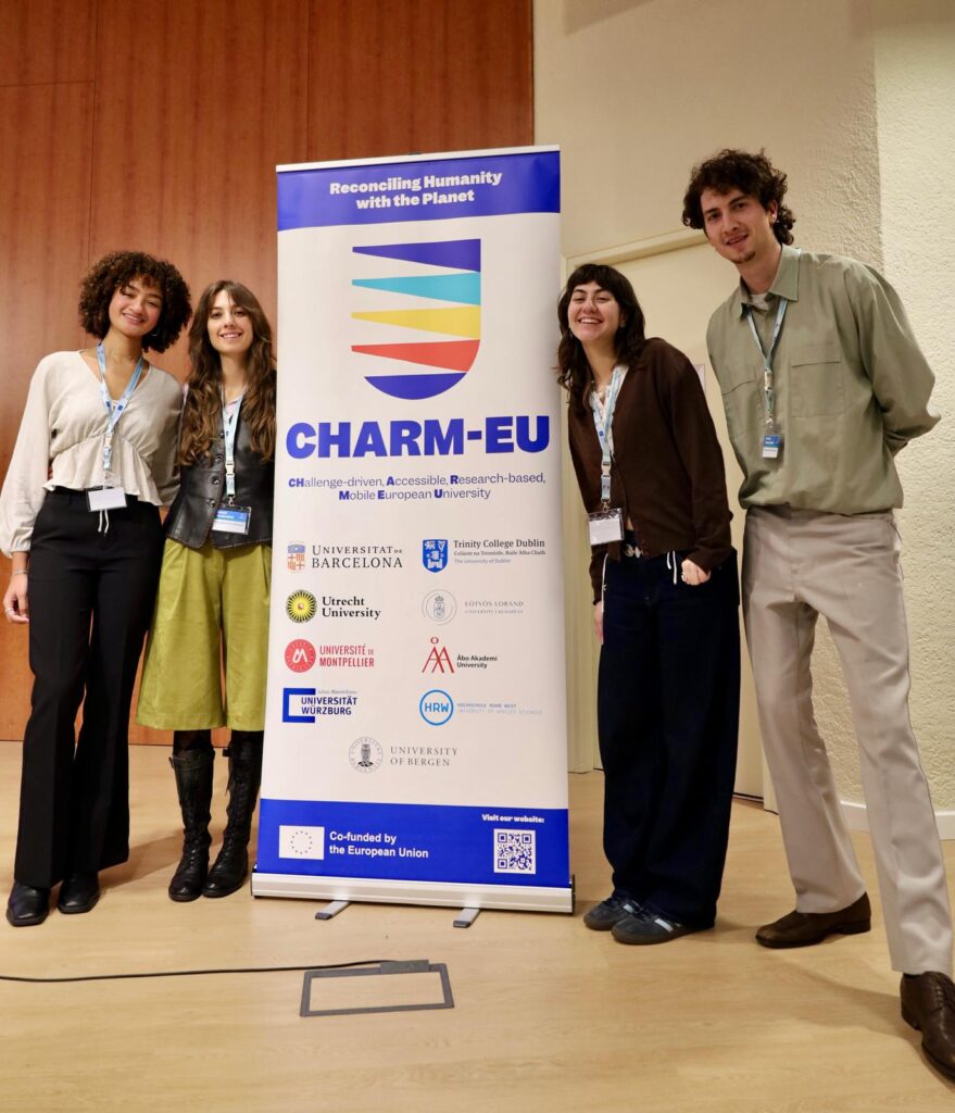 our students—Camille Dedeaux, Phoebe Sacares, Maria Hämäläinen, and Esra Nijman—standing next to a CHARM-EU banner.