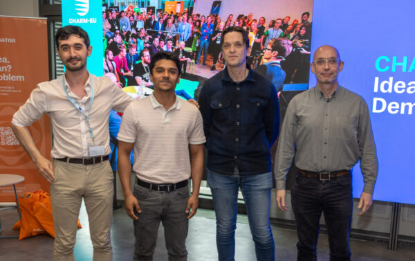 Four people stand together in front of a large screen