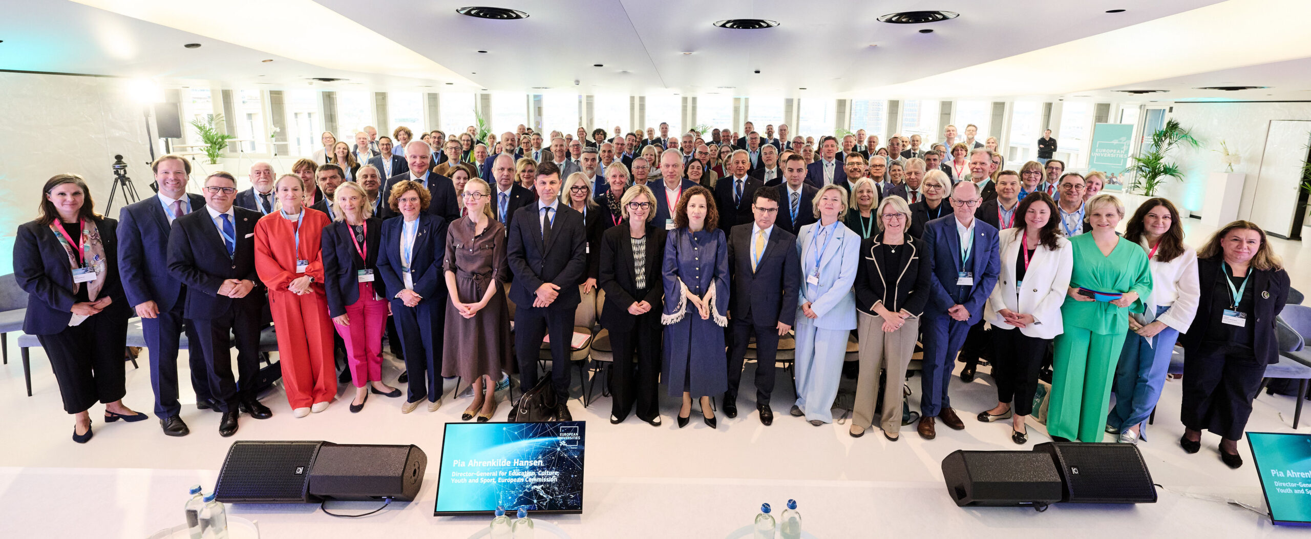 Large group of participants posing together at a European University event in a bright conference venue.
