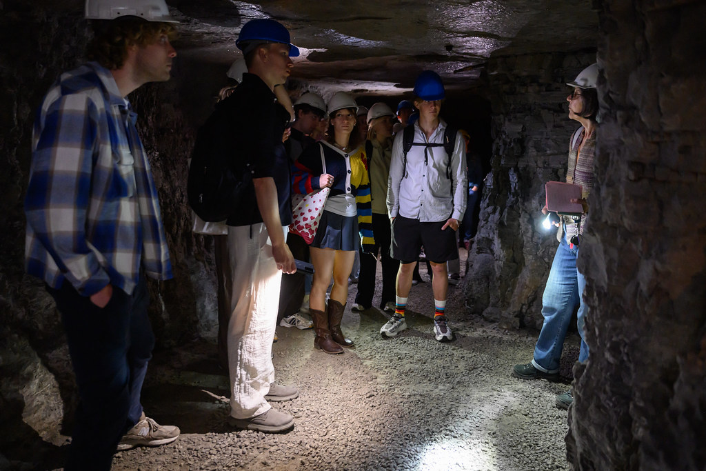 Students wearing safety helmets listening to a guide inside an underground mine tunnel.