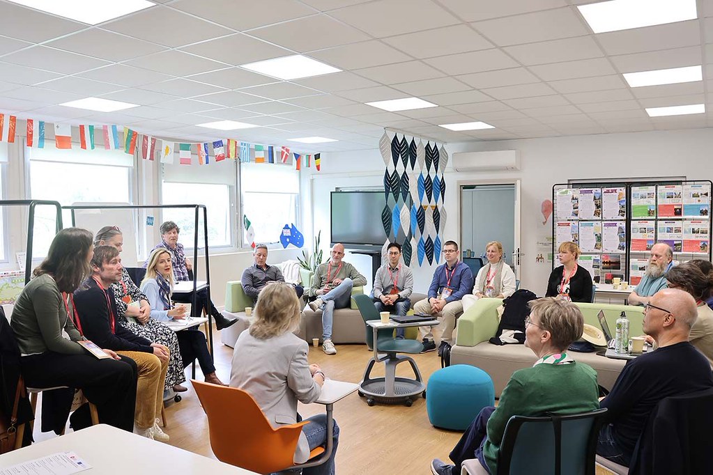 Participants seated in a circle during a CHARM‑EU discussion session in a classroom with international flags displayed.