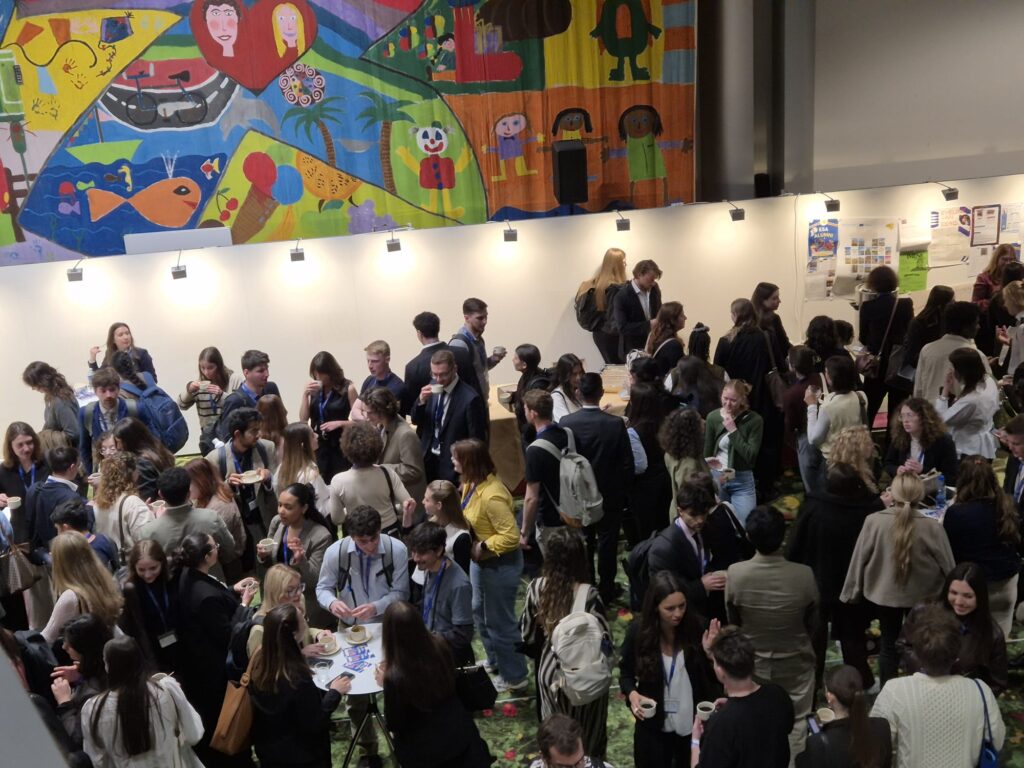 Participants networking during a conference reception beneath a colourful mural.