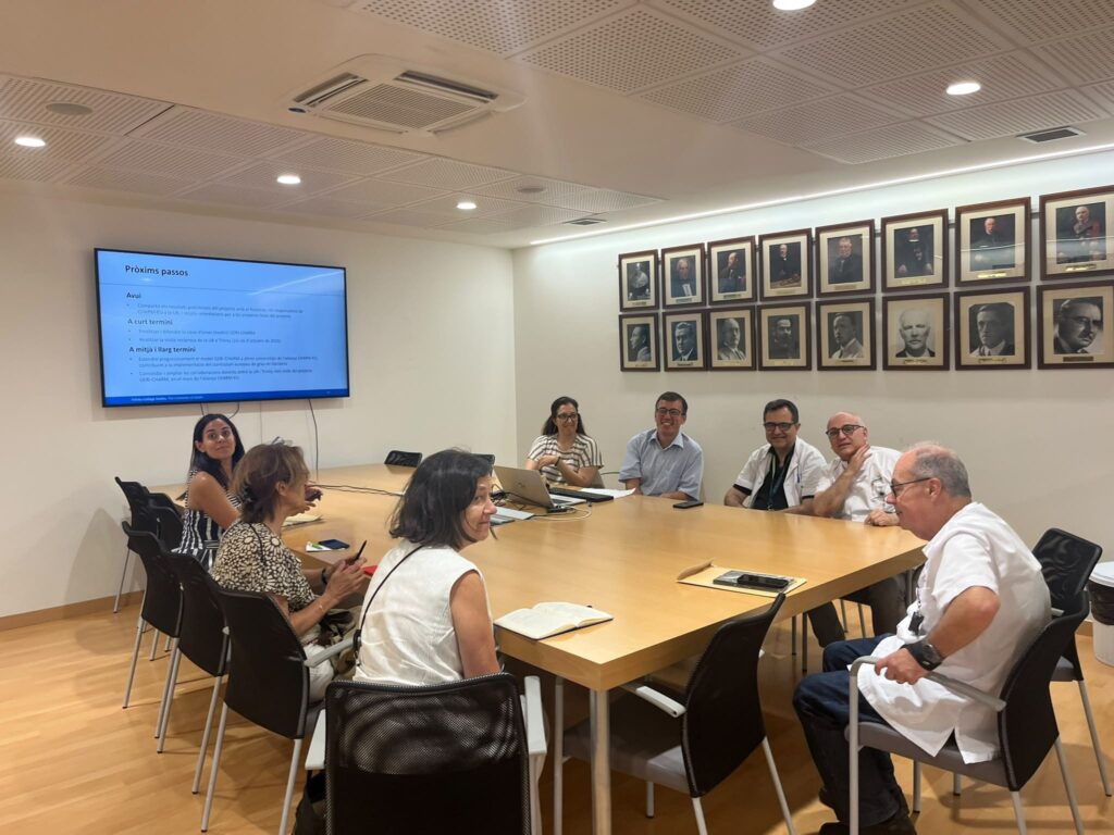 Participants seated around a meeting table during a discussion session, with a presentation screen in the background.