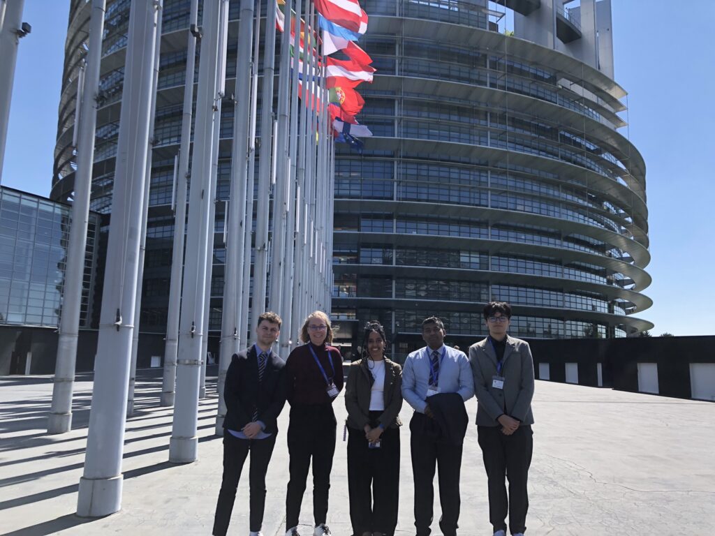 Participants standing outside the European Parliament building beneath EU member state flags.