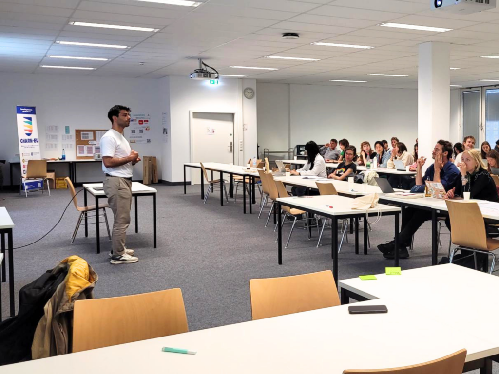 Speaker presenting to participants in a classroom with a PowerPoint presentation in the background.