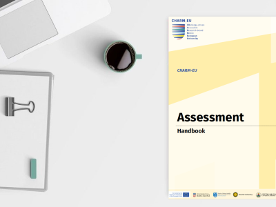 Picture of the laptop, booknote and coffee on a table together with the Assessment Handbook