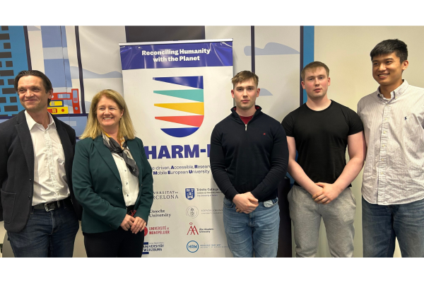 Photo: 5 participants of the CHARM-DEN 2024 with the CHARM-EU roll up at the Trinity College Dublin. Text: CHARM-DEN International Pitches 2024 CHARM-EU logo