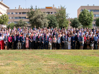 A large group of people pose for a group photo in an outdoor park setting with trees and apartment buildings in the background.