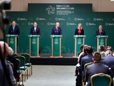 Five speakers standing at podiums during a formal press conference, with EU‑themed backdrop and audience seated in front.