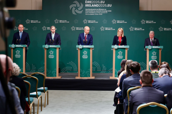 Five speakers standing at podiums during a formal press conference, with EU‑themed backdrop and audience seated in front.