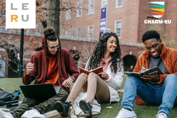 Photo: 3 university students, 2 boys and a girl, in the green grass of the university, with books in their hands smiling. Logos: LERU and CHARM-EU