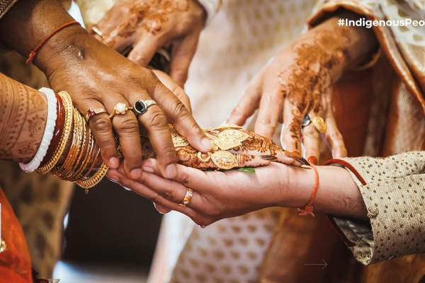 An image of people's clasped hands, richly adorned with henna and gold jewellery