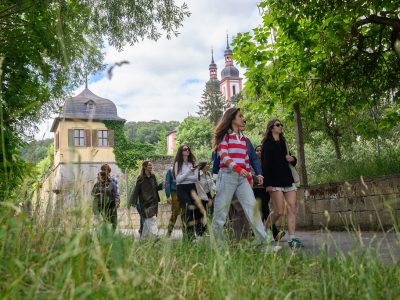 Group of students walking along a tree-lined path during an educational field visit, with historic buildings visible in the background.