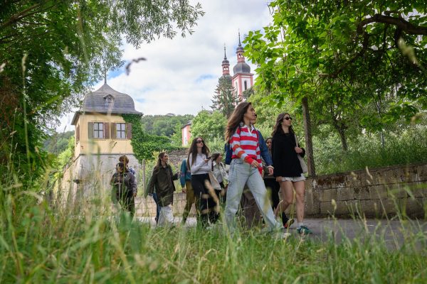 Group of students walking along a tree-lined path during an educational field visit, with historic buildings visible in the background.